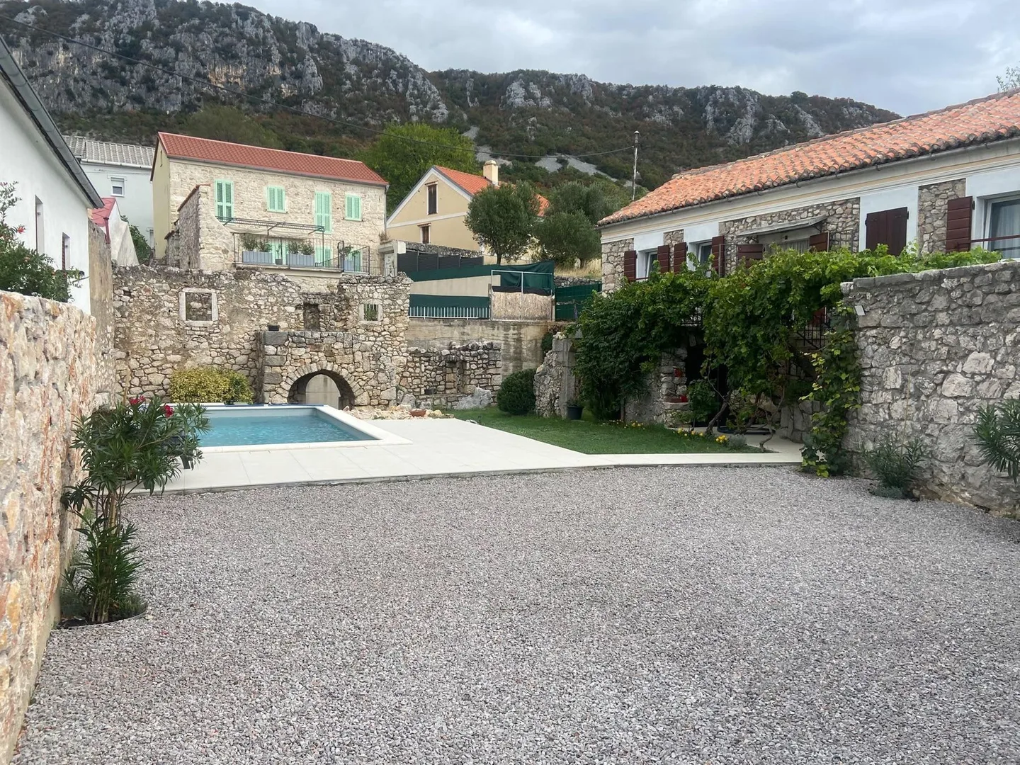 The courtyard from the gate: gravel, the pool and the ruin’s arch, the mountain behind
