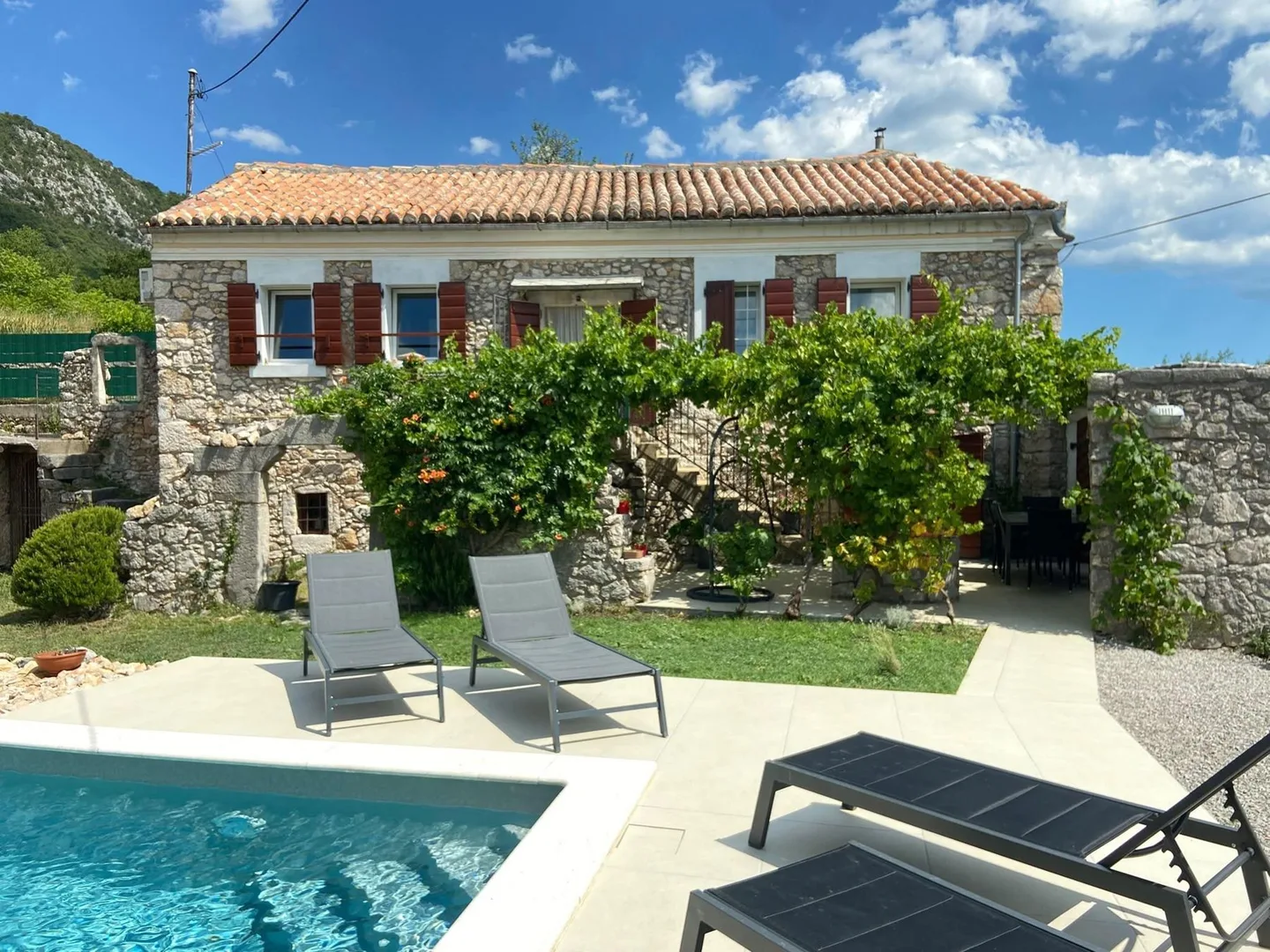 Loungers on the grass in front of the house, the pool in the foreground
