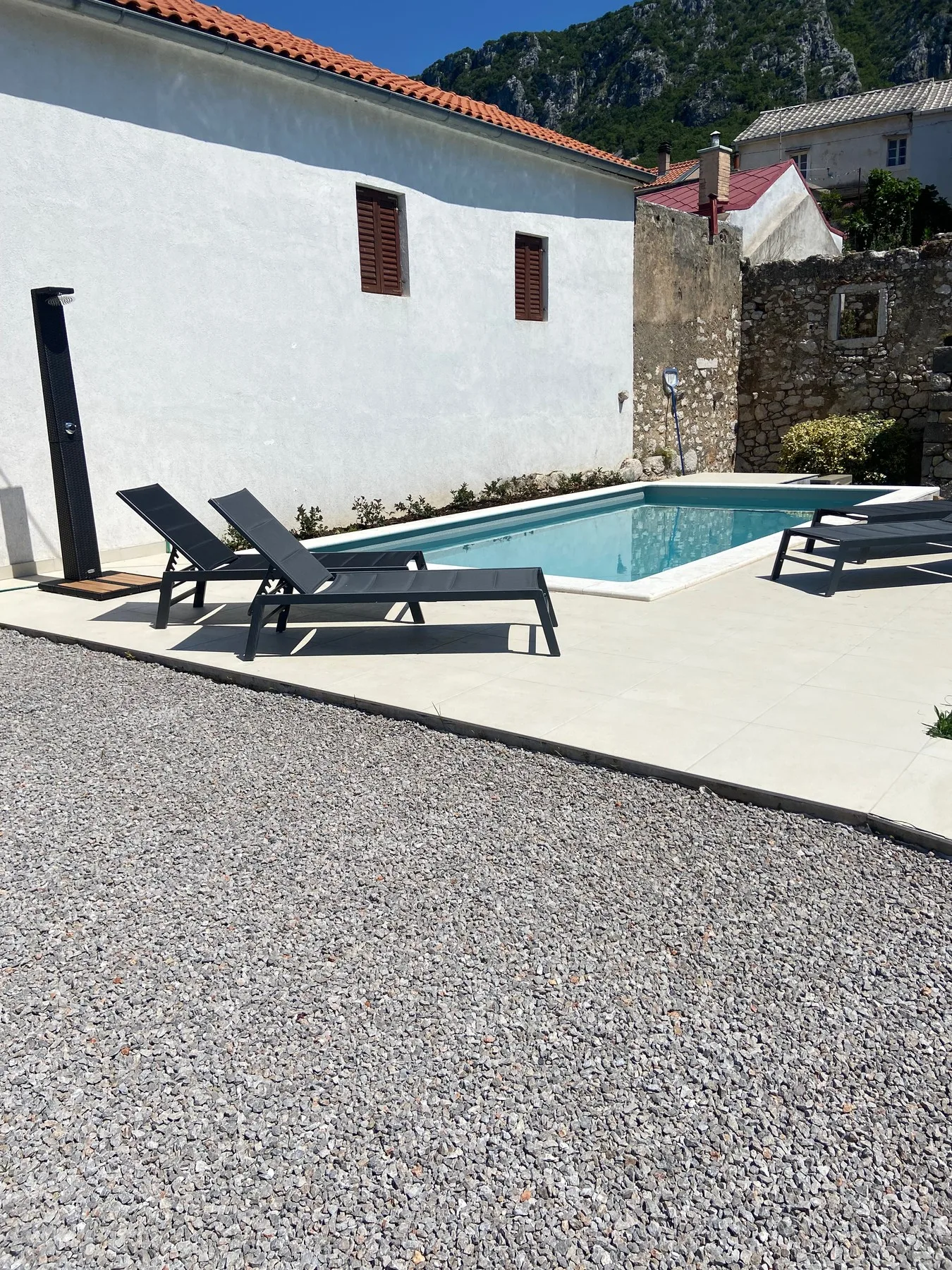 Loungers on the pale stone deck beside the pool, an outdoor shower against the white wall