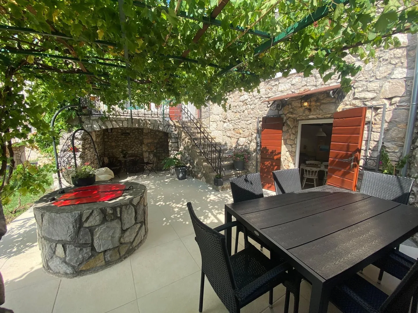 The terrace in one frame: the table under the vine, the stone well with its red lid and the outside stairs