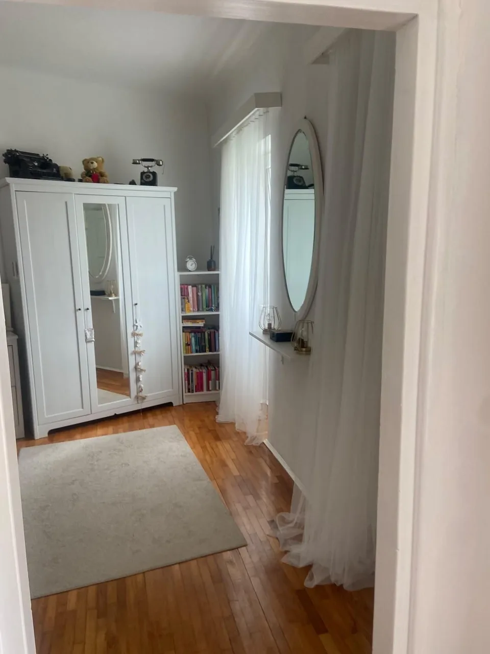 A white wardrobe and an oval mirror off the hallway